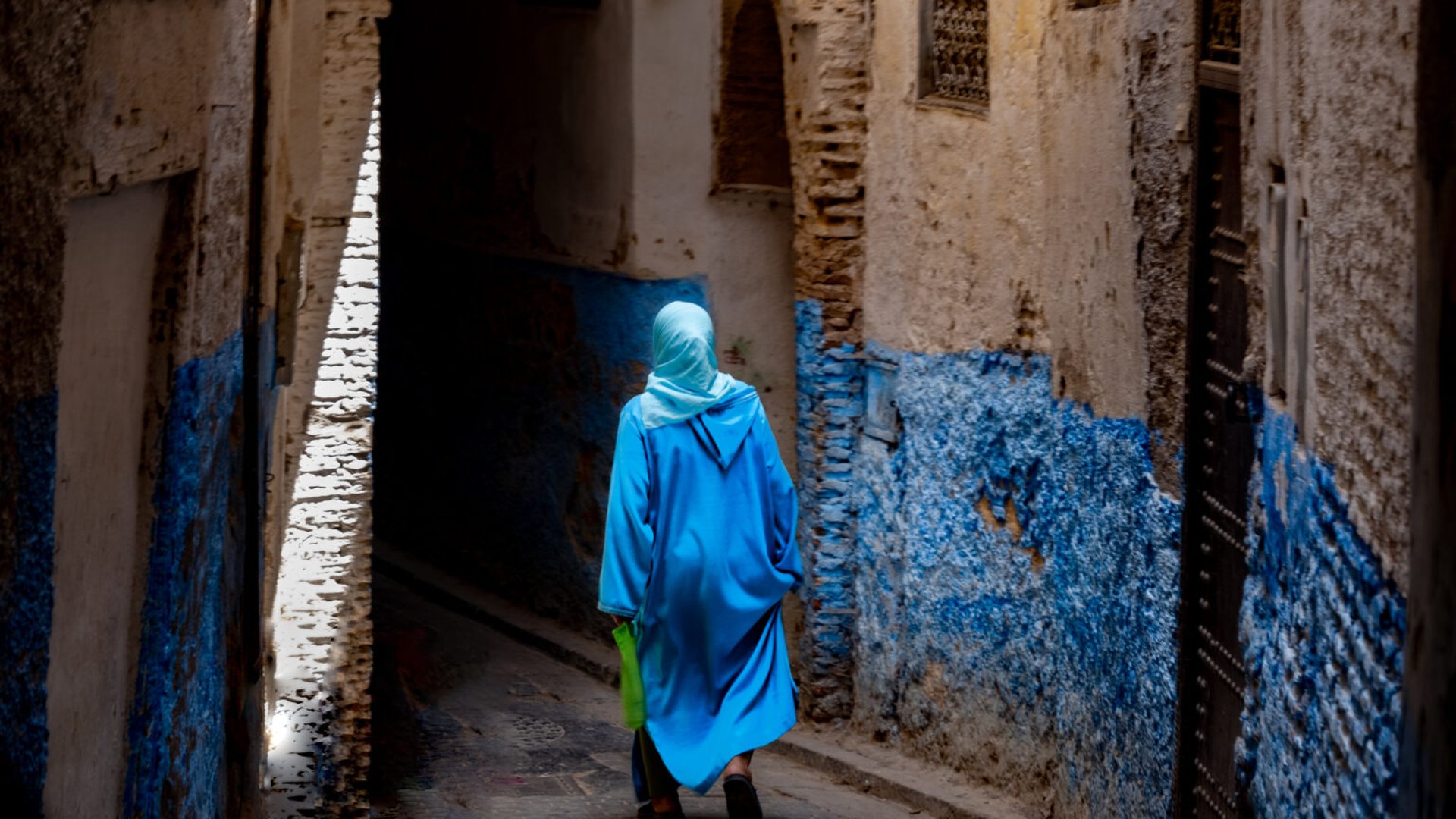 Fes medina narrow alley blue djellaba man carrying